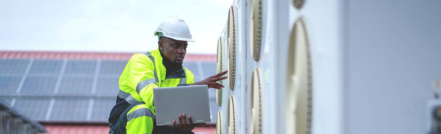 Technician with laptop reviewing equipment on a rooftop