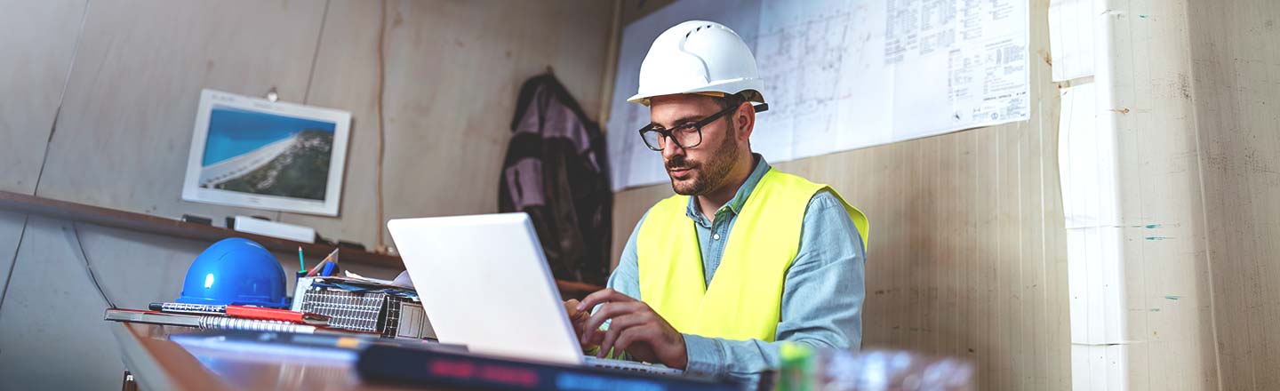 Engineer reviewing plans at a desk with a laptop